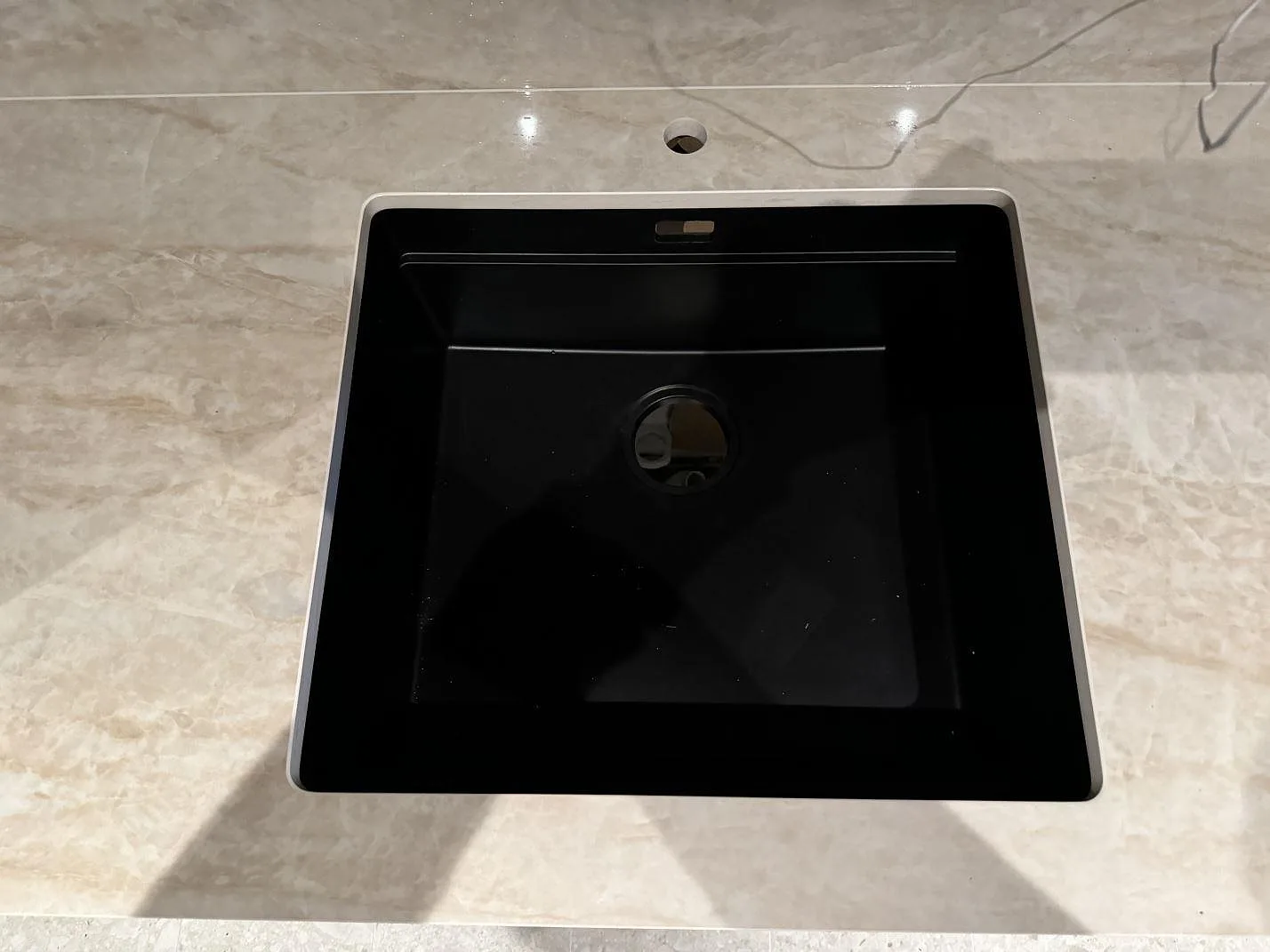 Ovanvy av svart diskho i en köksbänkskiva av polerad Dekton Arga med blandarhål och blank ådrad yta i Höllviken.