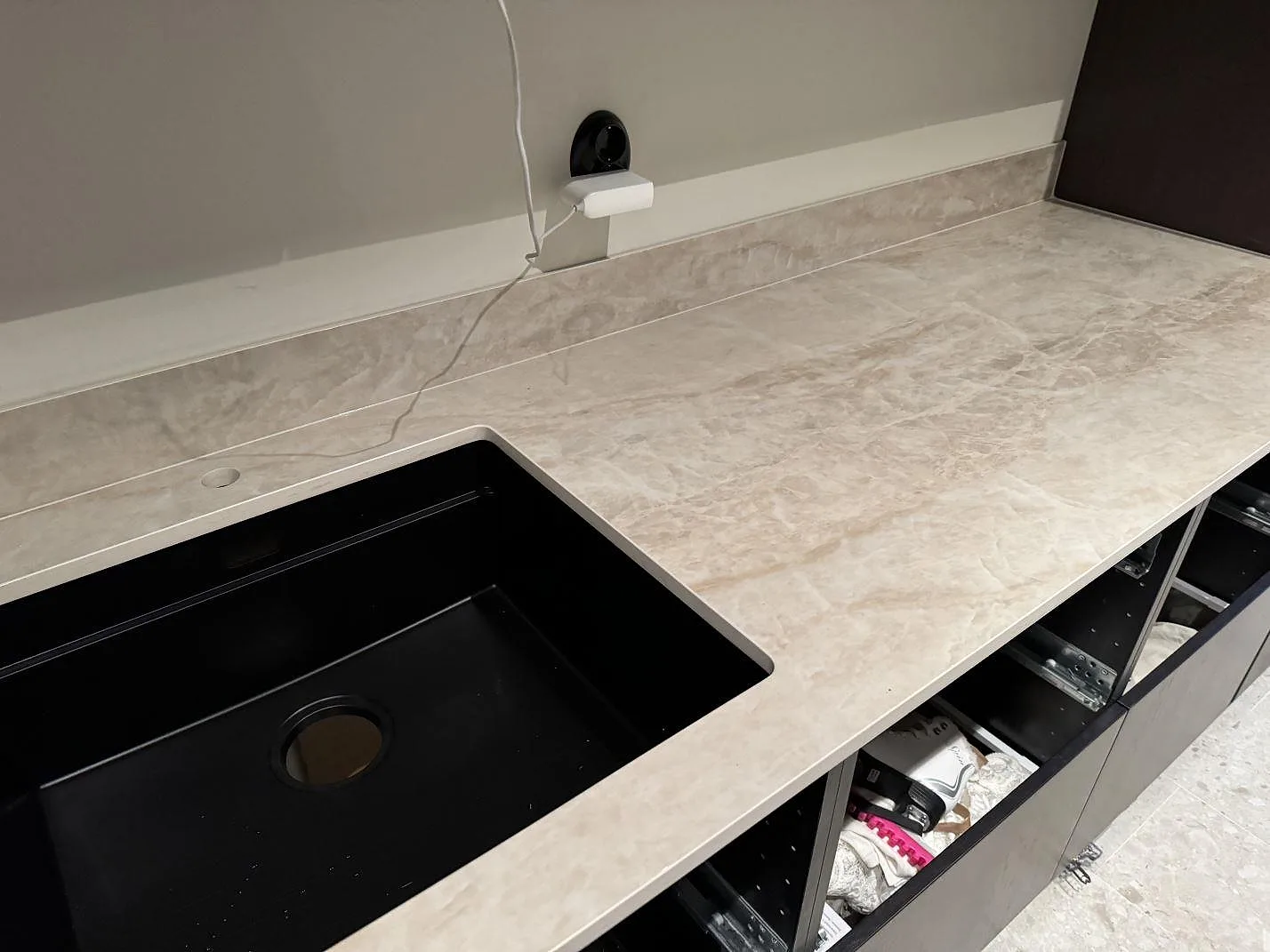 L-formad köksbänkskiva i polerad Dekton Arga med svart övermonterad diskho, mörkbruna stommar och stänkskydd i Höllviken.