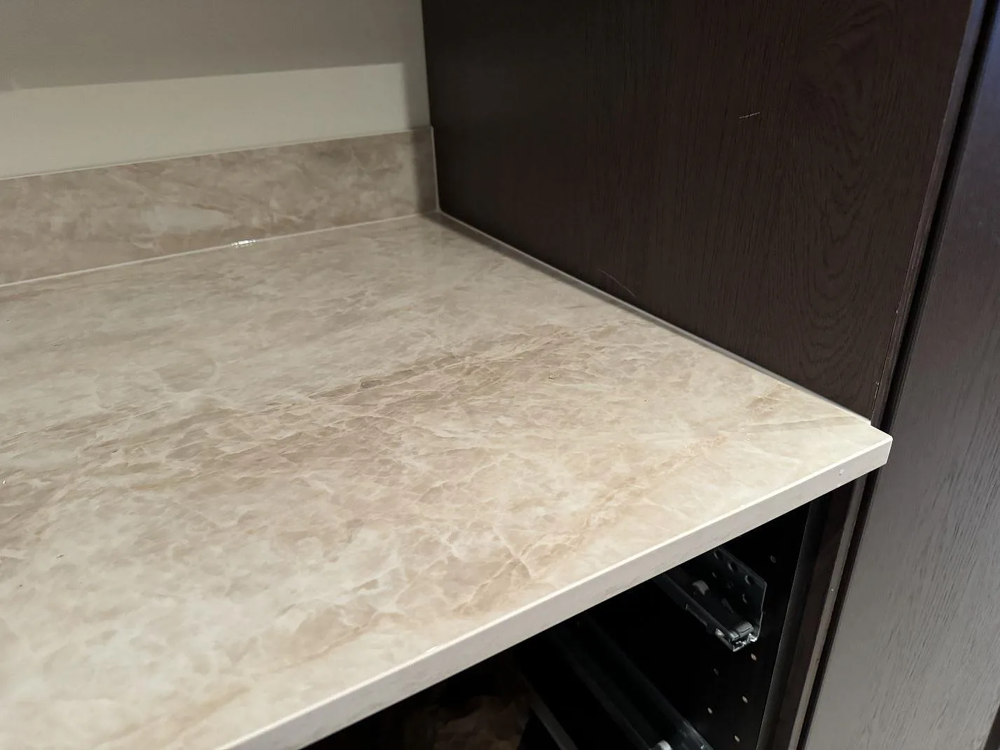 Närbild på kant och stänkskydd i polerad Dekton Arga, monterat mot mörkbruna köksstommar i Höllviken.