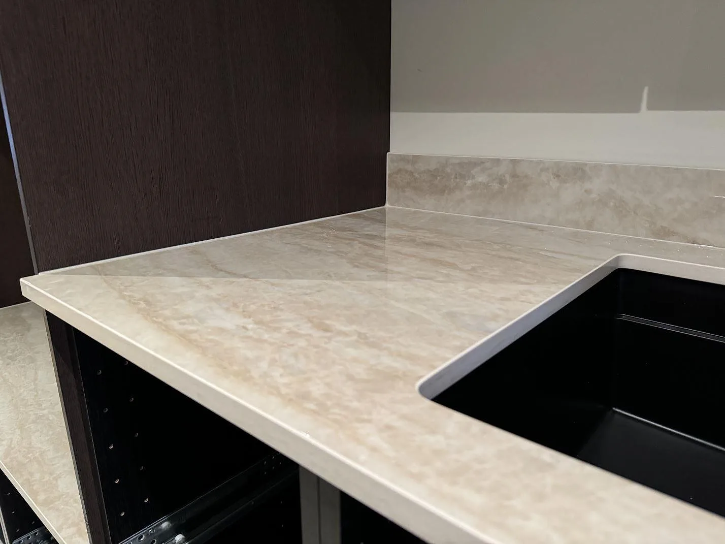 Närbild på polerad Dekton Arga runt den svarta diskhon, med ljus beige ådring och mörkbruna köksstommar i Höllviken.