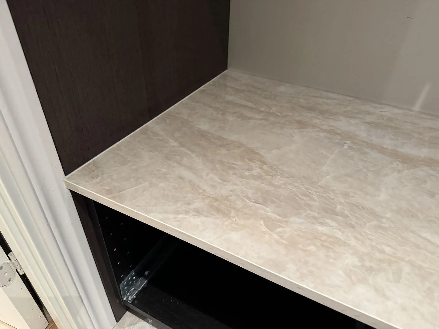 Detalj av polerad Dekton Arga bänkskiva med ljus travertinliknande ådring mot mörkbrun köksinredning i Höllviken.