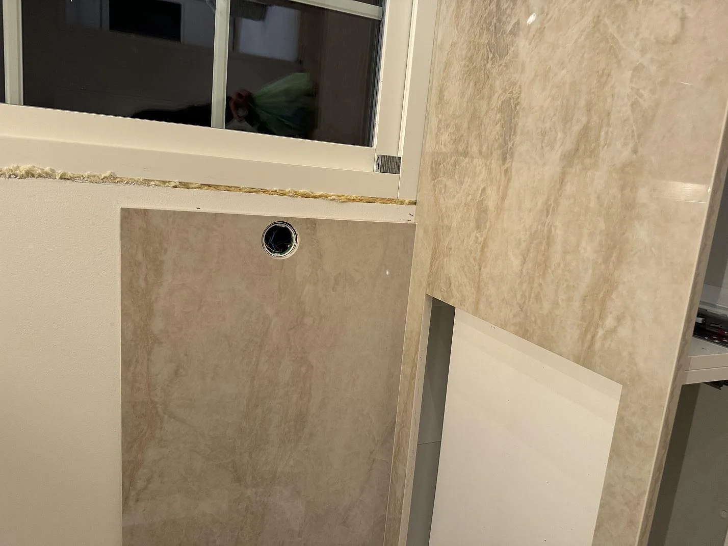 Polerad Dekton Arga keramik som bänkskiva och vertikal väggskiva med runt hål vid fönster i Höllviken.