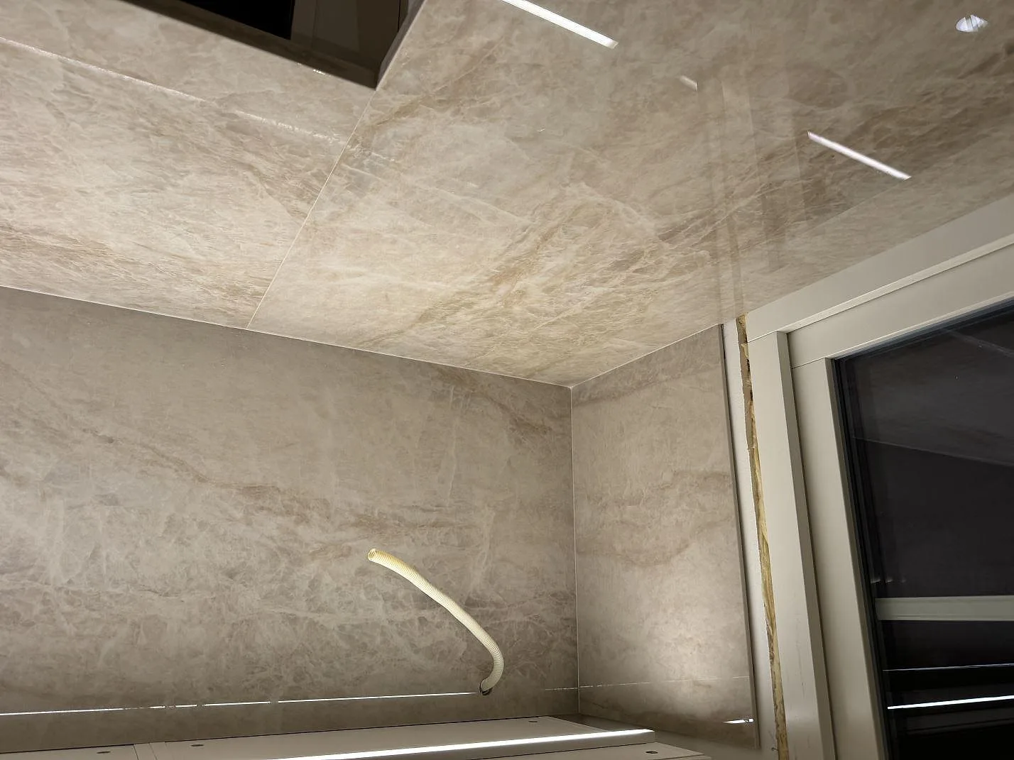 Väggbeklädnad och bänkskiva i polerad Dekton Arga keramik i hörn med installationsslang i Höllviken.