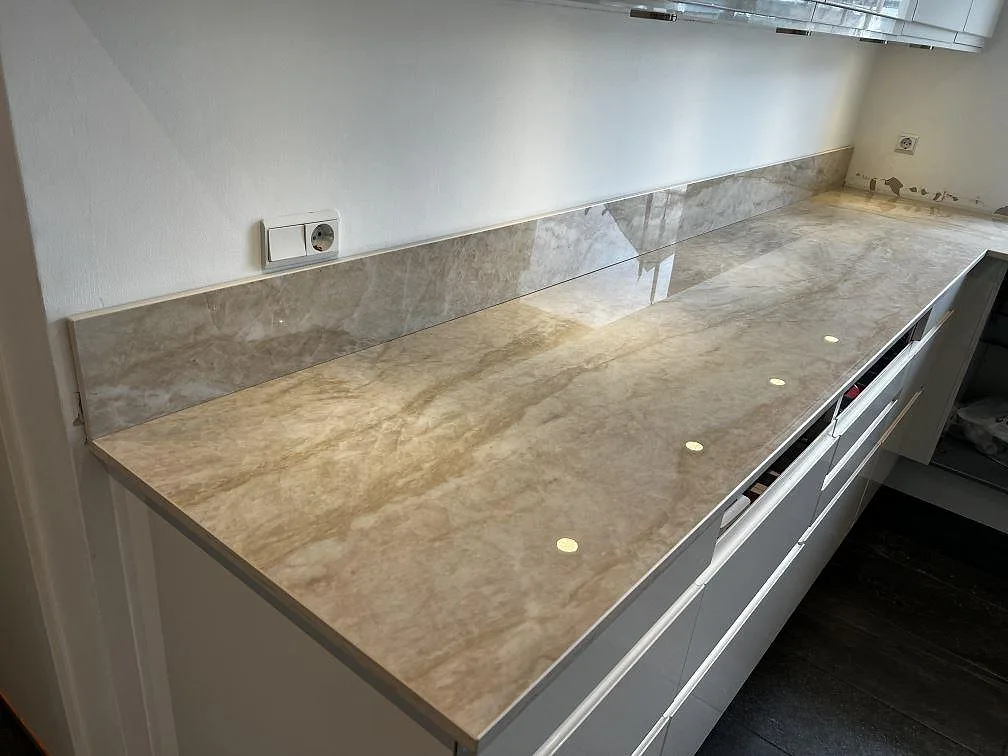 Polerad köksbänkskiva i Dekton Arga med matchande stänkskydd och vita underskåp i Hörby.