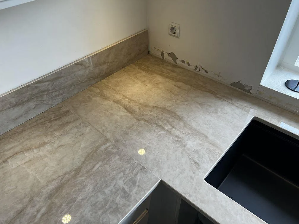 Hörnsektion i polerad Dekton Arga keramik med stänkskydd och svart underlimmad diskho vid fönster i Hörby.
