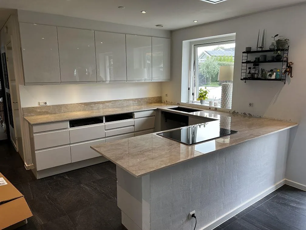 U-format kök med köksö, polerad köksbänkskiva i Dekton Arga keramik och vita skåp i Hörby.