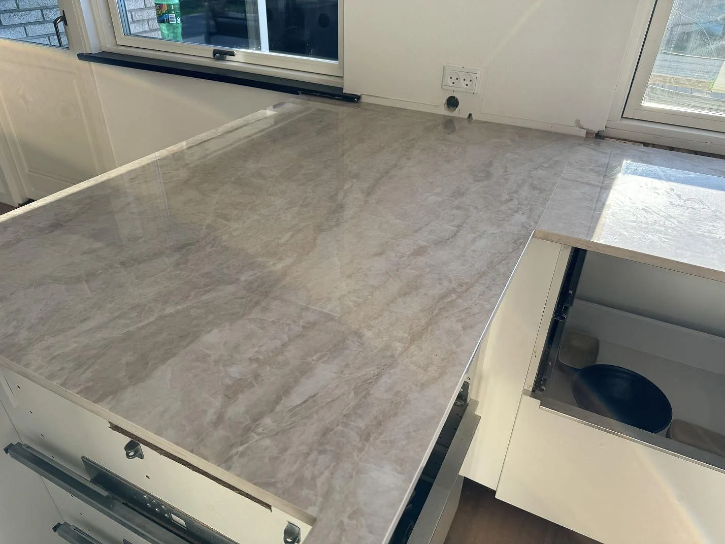 Polerad köksbänkskiva i Dekton Arga längs fönsterväggen, med blank yta och öppna skåpstommar i Hørsholm.