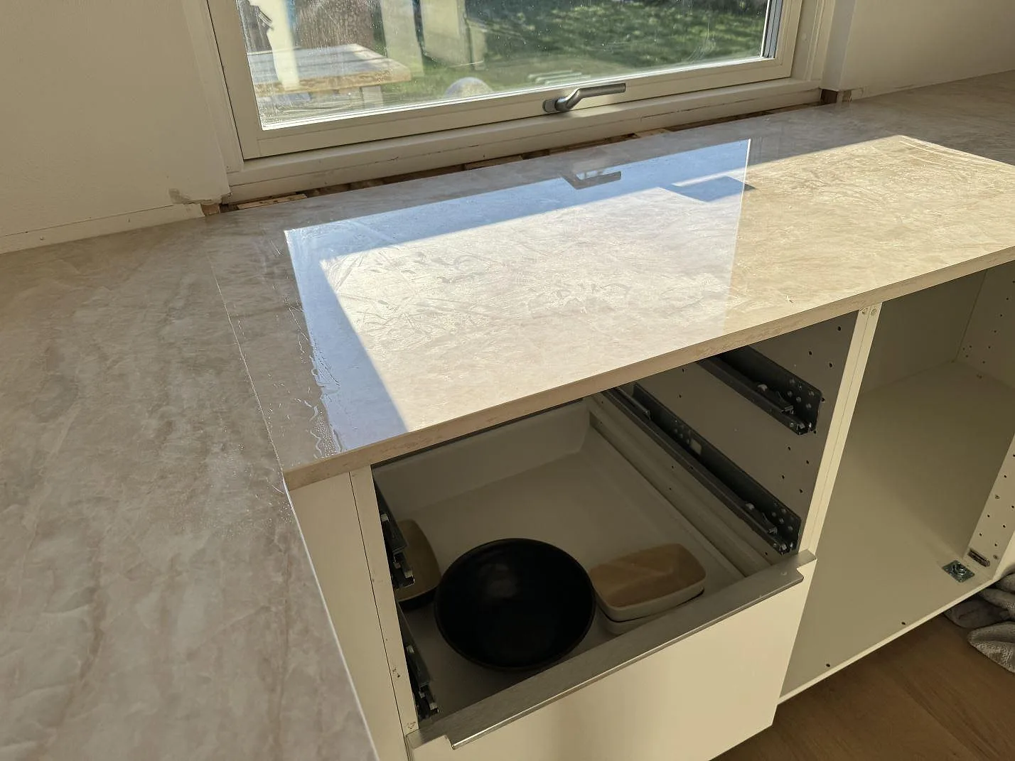 Köksbänkskiva i polerad Dekton Arga vid fönster, med reflekterande yta och öppen skåpstomme i Hørsholm.