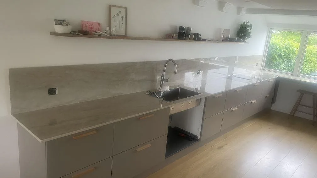 Köksbänkskiva i polerad Dekton Arga keramik med rostfri diskho, häll och matchande stänkskydd i ett kök i Holte.