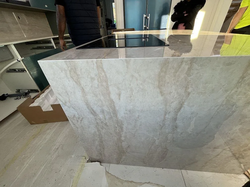 Köksö med vattenfallsida i polerad Dekton Arga keramik och infälld häll under montering i ett kök i Huddinge.