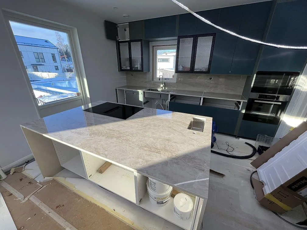 Köksbänkskiva och köksö i polerad Dekton Arga keramik med häll, rostfri diskho och mörkt grönblå skåpsluckor i Huddinge.