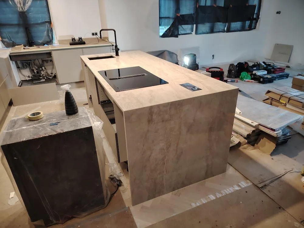 Köksö i polerad Dekton Arga, 20 mm keramik, med infälld induktionshäll i ett kök under montering i Huddinge.