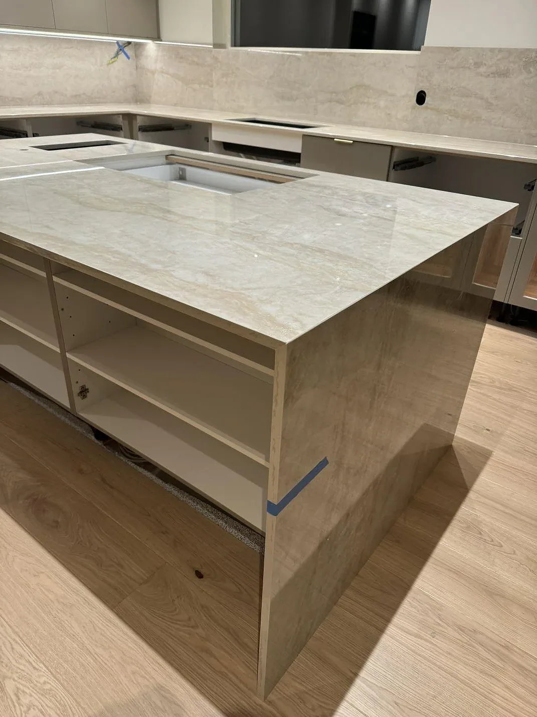 Vinklad vy av köksö och väggbänk i polerad Dekton Arga med ljus ådring under montering i Hunnebostrand.