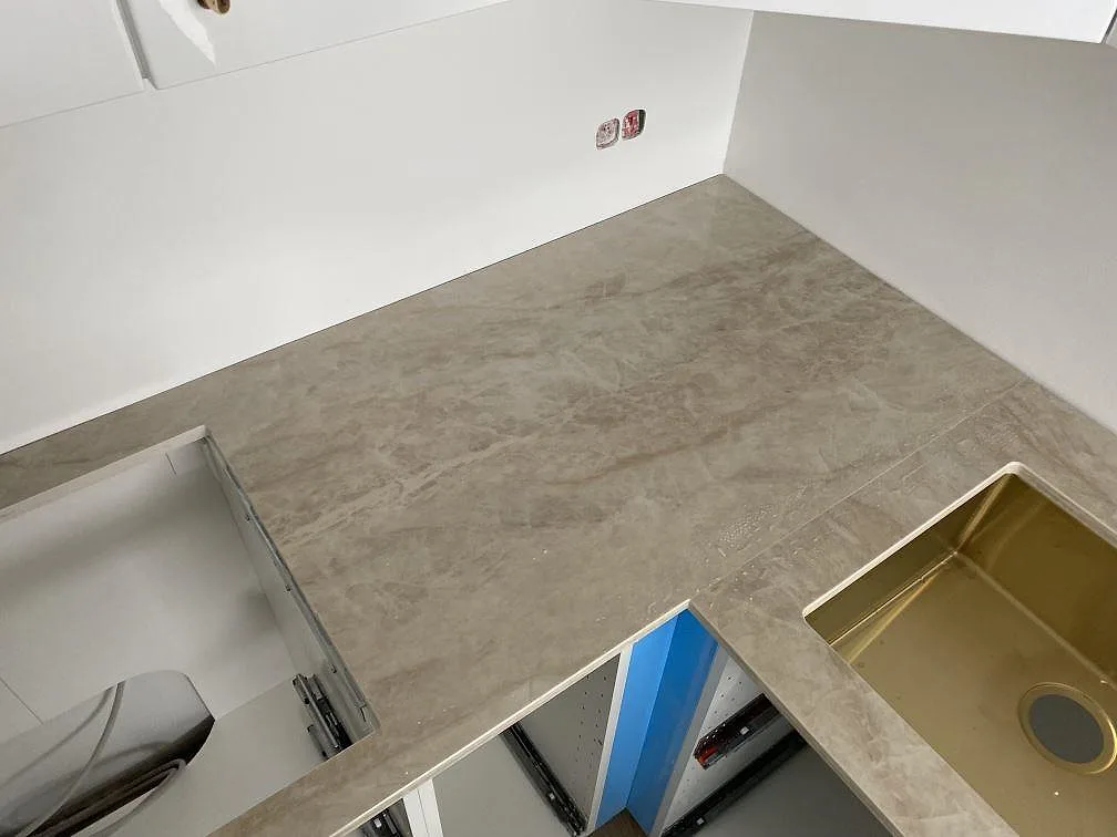 Polerad Dekton Arga bänkskiva i hörnform med beige ådring, synlig diskho och separat hällurtag i ett kök i Hvidovre.
