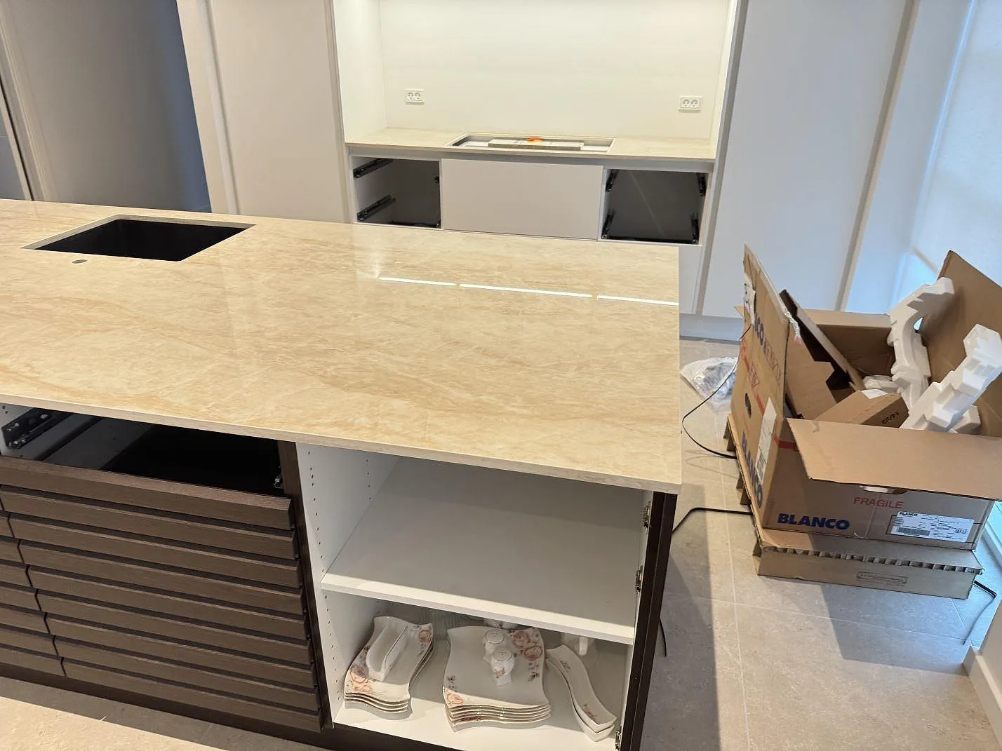 Bred köksö i polerad Dekton Arga med beige ådring, svart diskho och synlig väggbänk i ett kök i Hvidovre.