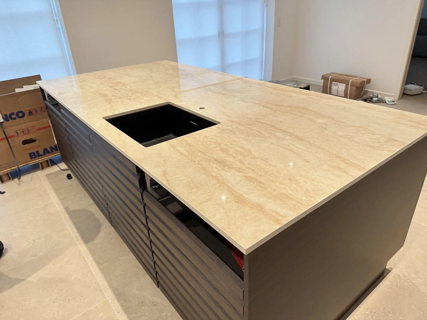 Köksö i polerad Dekton Arga med svart diskho och beige ådrad keramik i ett kök under montering i Hvidovre.