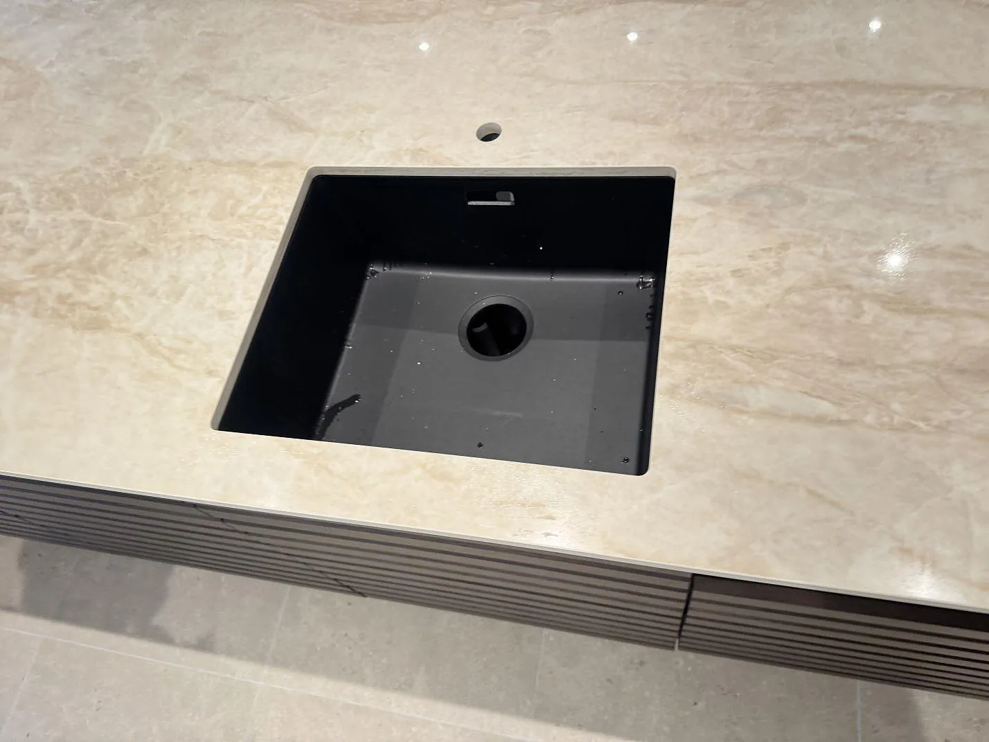 Närbild på svart diskho i en polerad Dekton Arga köksö med varm beige ådring i Hvidovre.