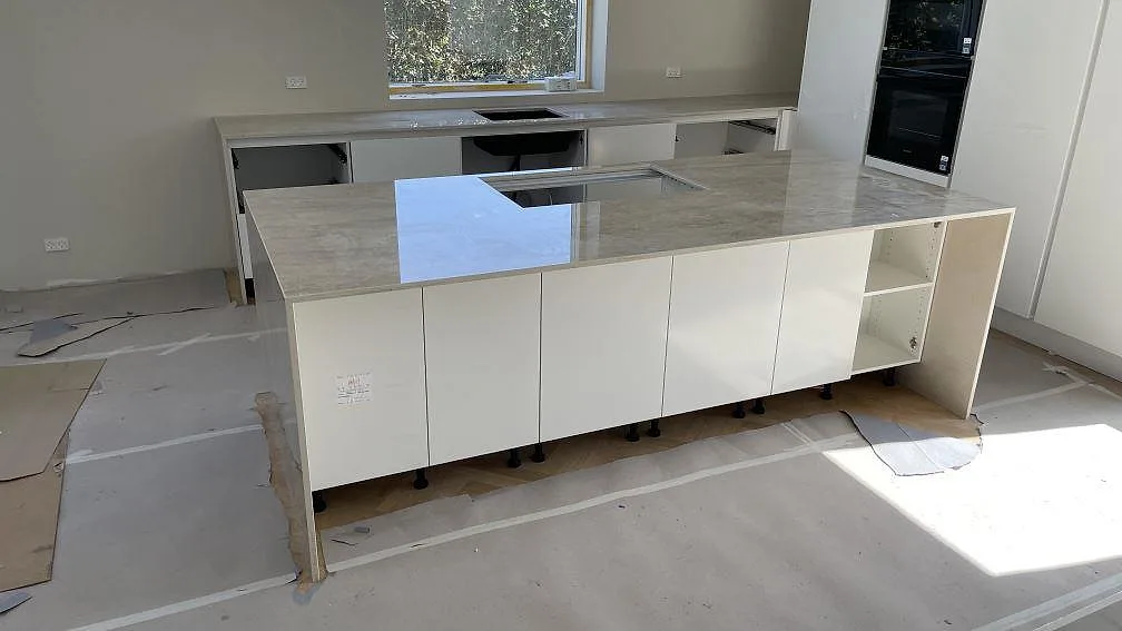 Köksbänkskiva i polerad Dekton Arga, keramik, med köksö och väggbänkar under montering i Ishöj.
