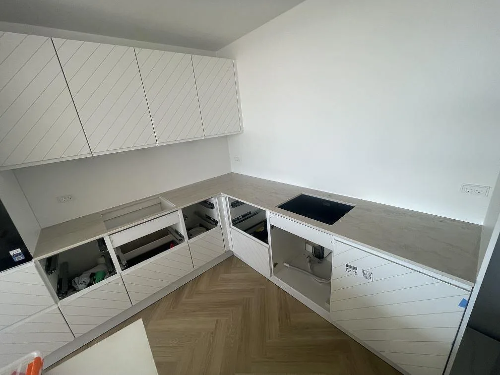 Köksbänkskiva i ljus Dekton Arga, polerad, monterad i L-form med underlimmad diskho och plats för induktionshäll i ett kök i Ishøj.