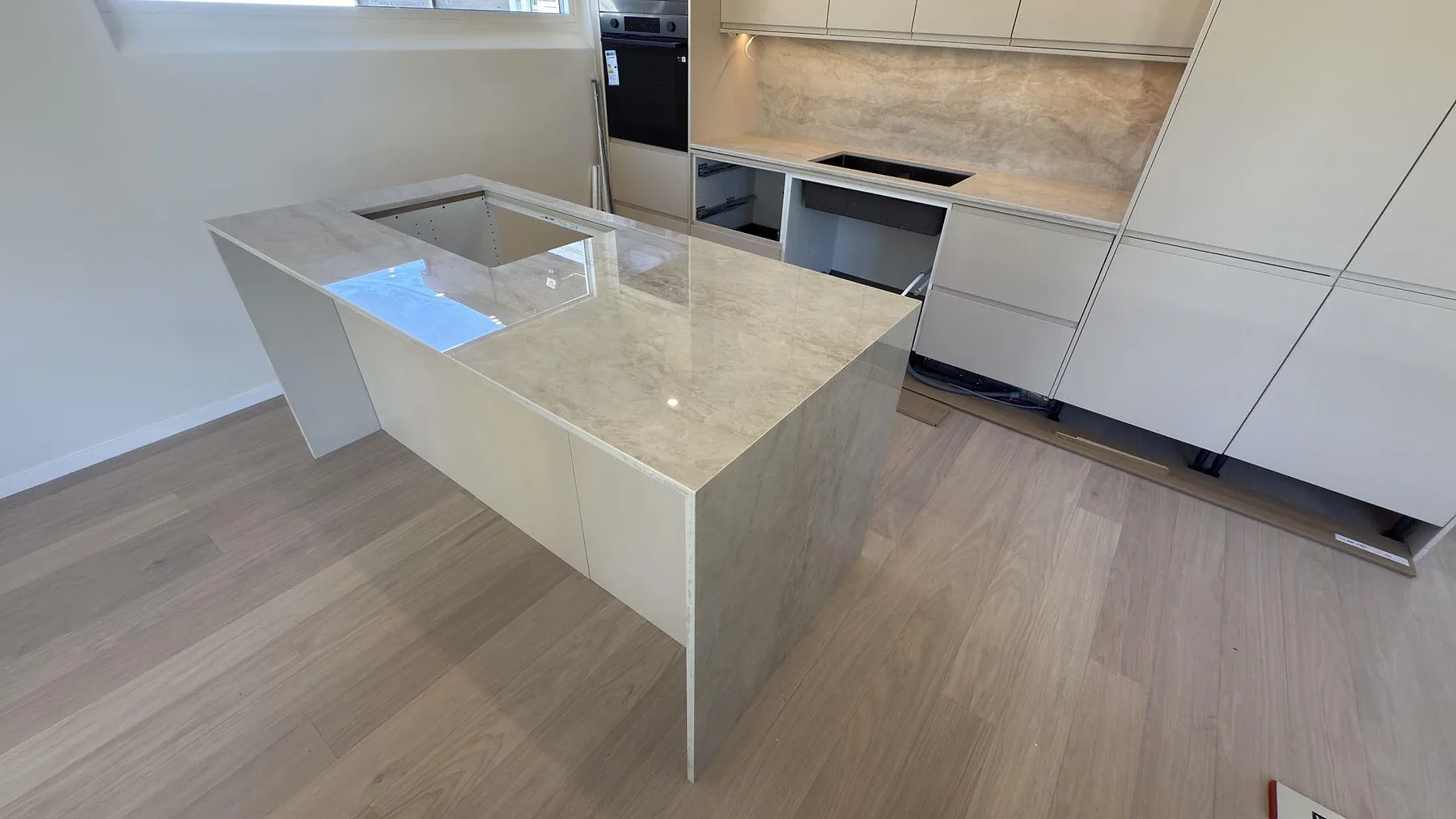 Köksbänkskiva i beige Dekton Arga, polerad keramik, på köksö i ett kök i Järfälla med matchande stänkskydd och plats för häll.