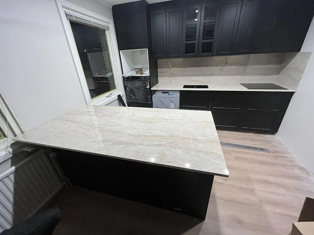 Polerad köksbänkskiva i Dekton Arga med ljus marmorering, halvö och matchande stänkskydd i ett mörkt kök i Jönköping.