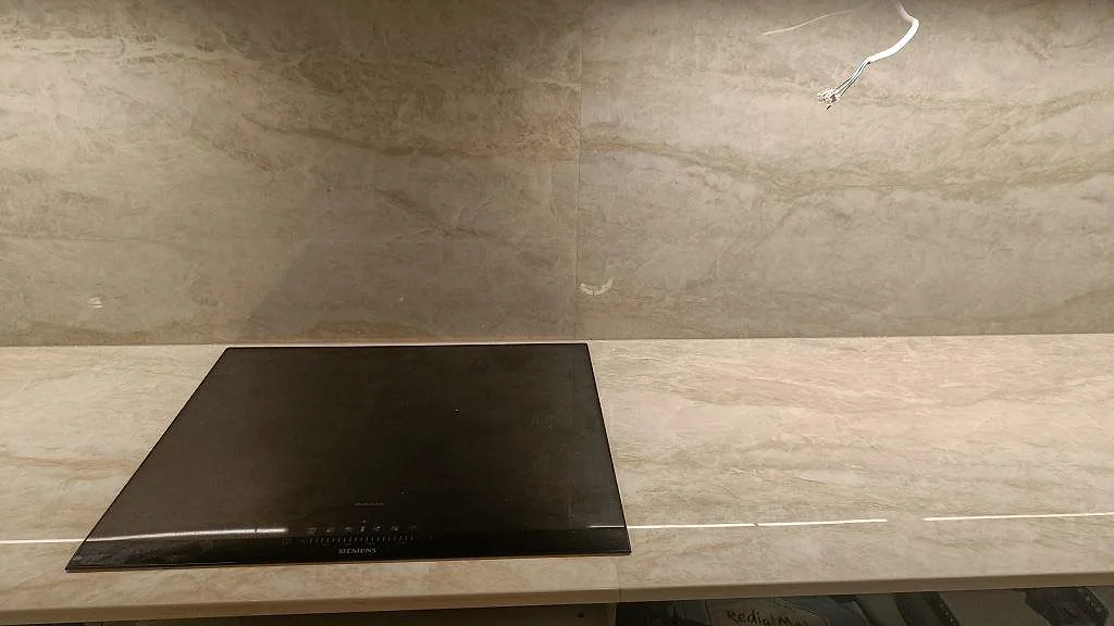 Induktionshäll på en köksbänkskiva i polerad Dekton Arga med stänkvägg i samma ljusa sten i ett kök i Kalmar.
