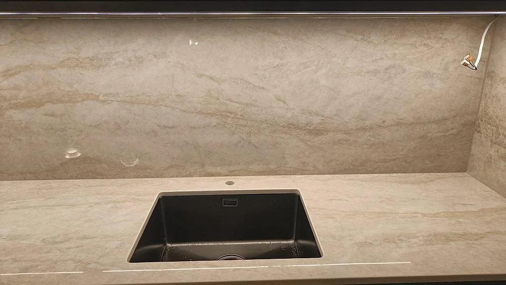 Underlimmad diskho i en polerad Dekton Arga köksbänkskiva med stänkvägg i samma sten i ett kök i Kalmar.