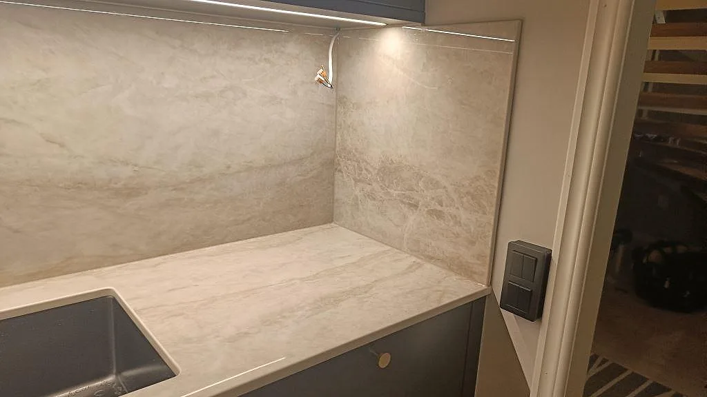 Köksbänkskiva i Dekton Arga med diskho och uppvikt stänkvägg i samma ljusa sten i ett kök i Kalmar.