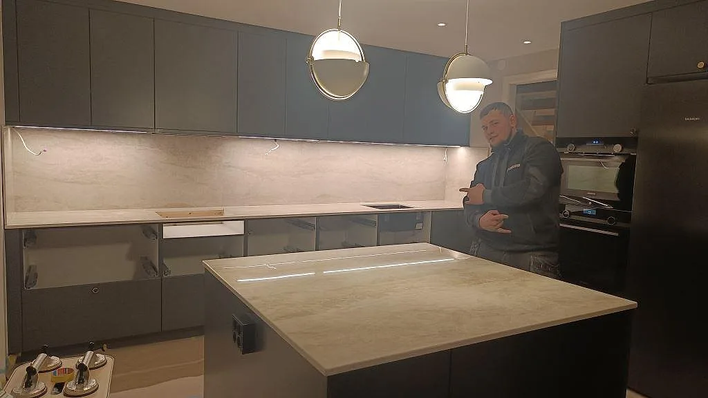Köksbänkskiva och köksö i polerad Dekton Arga under montering, med ljus ådring och heltäckande stänkskydd i ett kök i Kalmar.