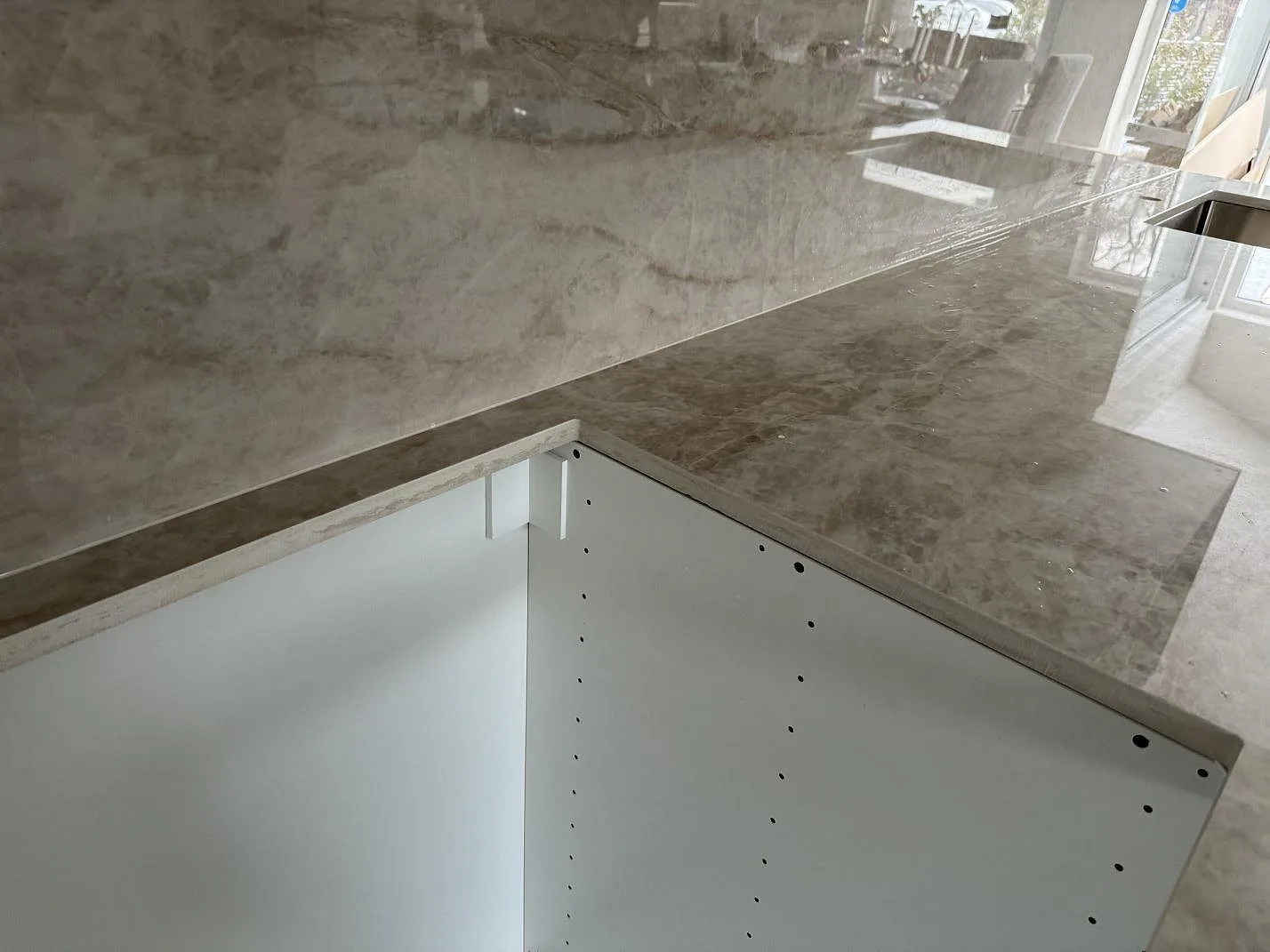 L-format hörn i polerad Dekton Arga med matchande väggbeklädnad och öppen vit köksstomme i Kalmar.