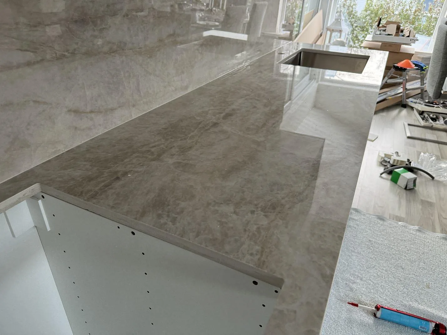 Lång köksbänkskiva i polerad Dekton Arga keramik med diskho och blank stänkyta under montering i Kalmar.