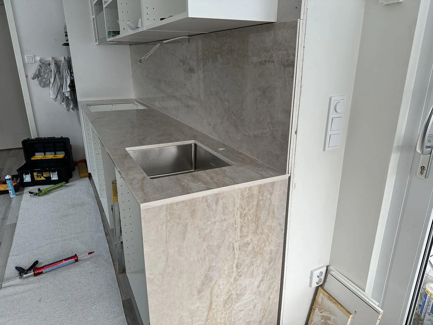 Köksbänkskiva i polerad Dekton Arga med rostfri diskho, vit köksinredning och verktyg under montering i Kalmar.