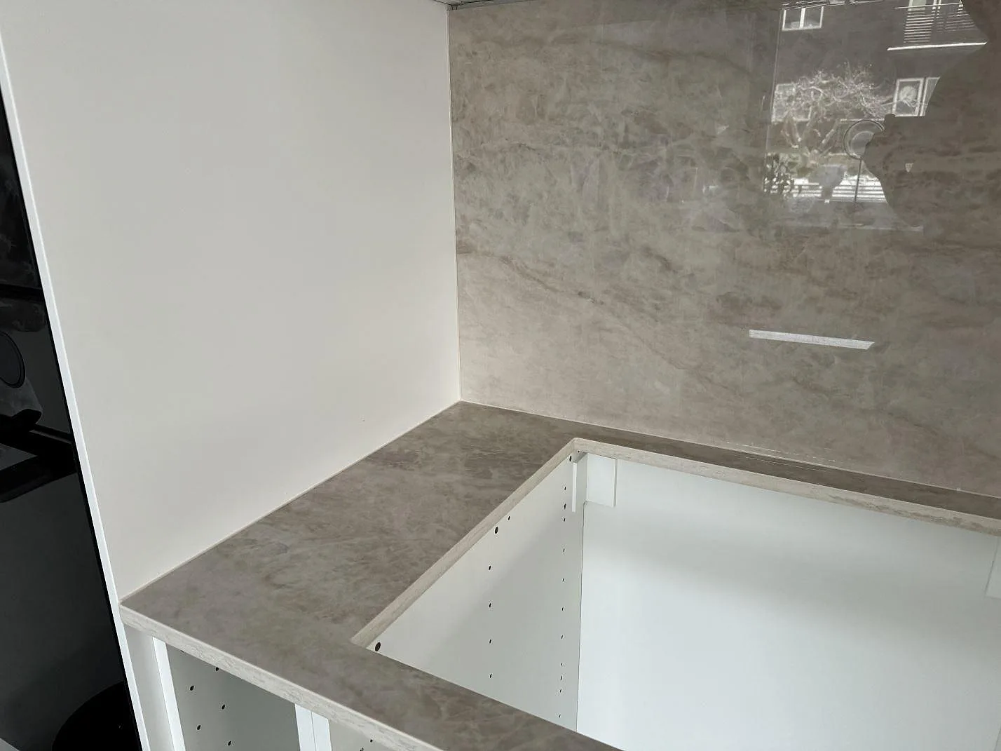 L-formad köksbänkskiva i polerad Dekton Arga med hög blank väggbeklädnad och vita köksstommar i Kalmar.
