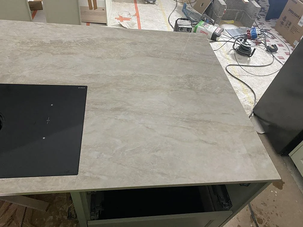 Sidovy av köksö i polerad Dekton Arga med svart häll och bred arbetsyta under montering i Kareby.