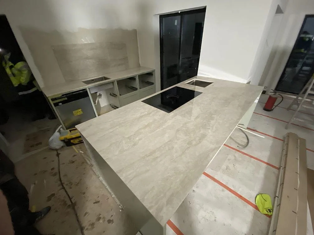 Köksbänkskiva och köksö i polerad Dekton Arga med ljus ådring, svart häll och rostfri diskho under montering i Kareby.