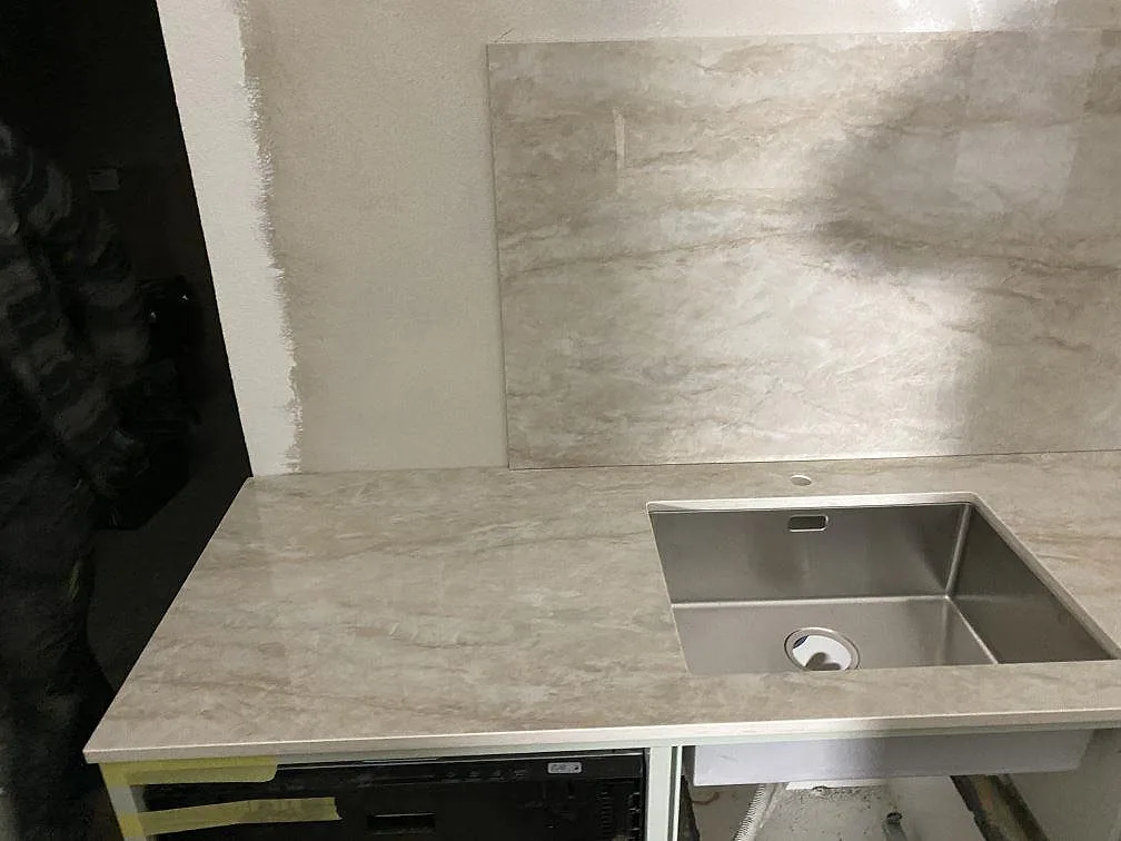 Detalj av polerad Dekton Arga vid rostfri diskho, med ljus keramikyta och stänkskydd i Kareby.