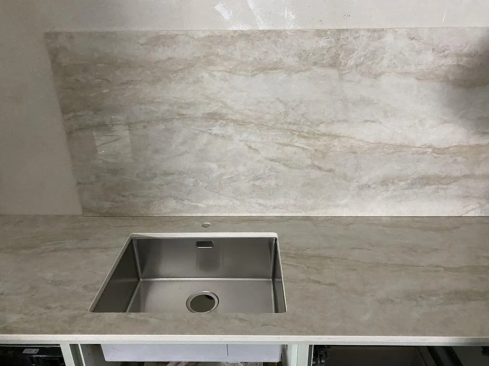 Köksbänkskiva i gräddvit Dekton Arga, polerad, med underlimmad rostfri diskho och stänkskydd i samma sten i ett kök i Kareby.