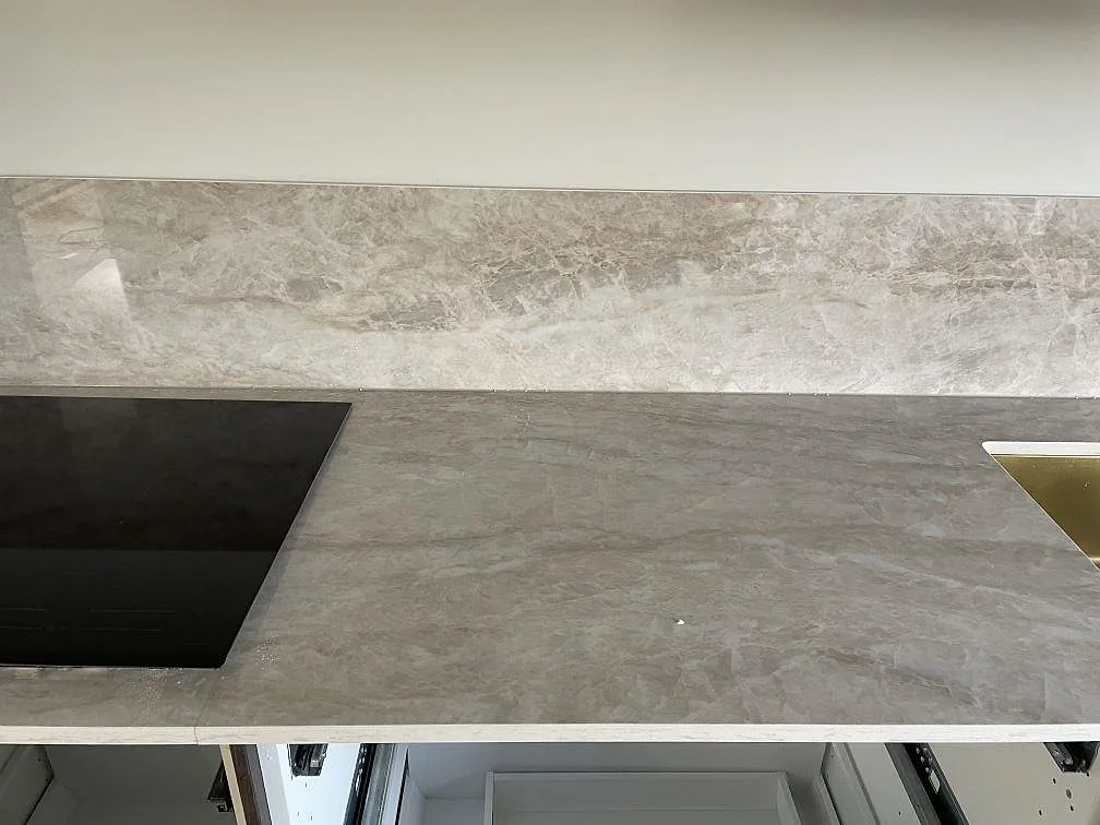 Köksbänkskiva i polerad Dekton Arga, keramik, med svart häll, guldfärgad diskho och 8 mm stänkskydd i ett kök i Karlshamn.
