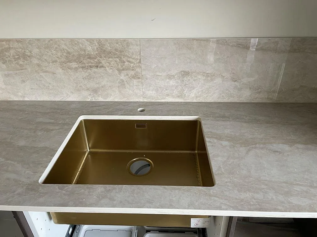 Guldfärgad diskho i polerad Dekton Arga köksbänkskiva med matchande stänkskydd under montering i Karlshamn.