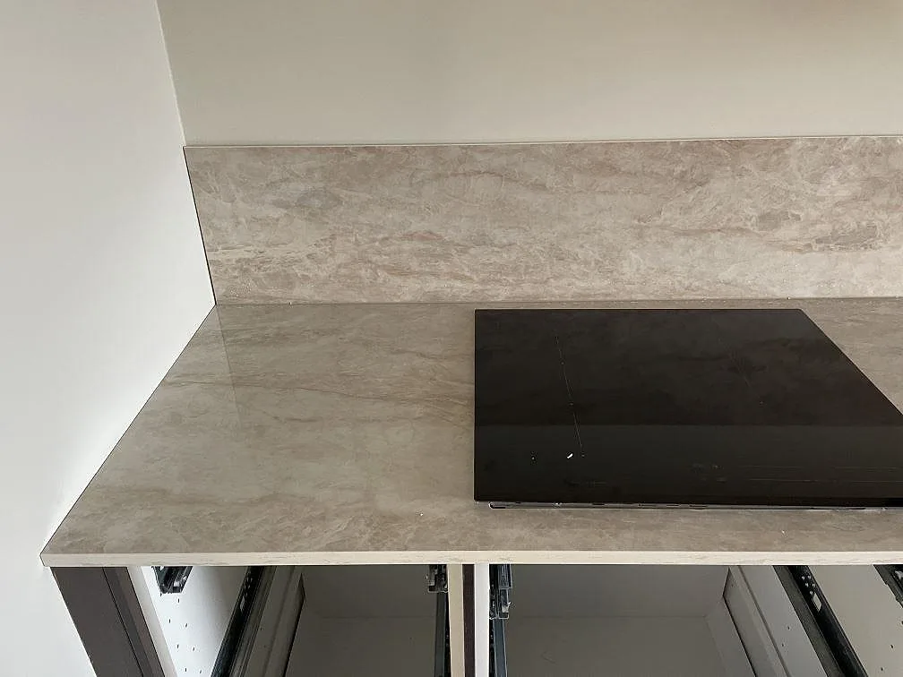 Svart häll i polerad Dekton Arga bänkskiva med gråbeige ådring och låg stänkkant i kök i Karlshamn.