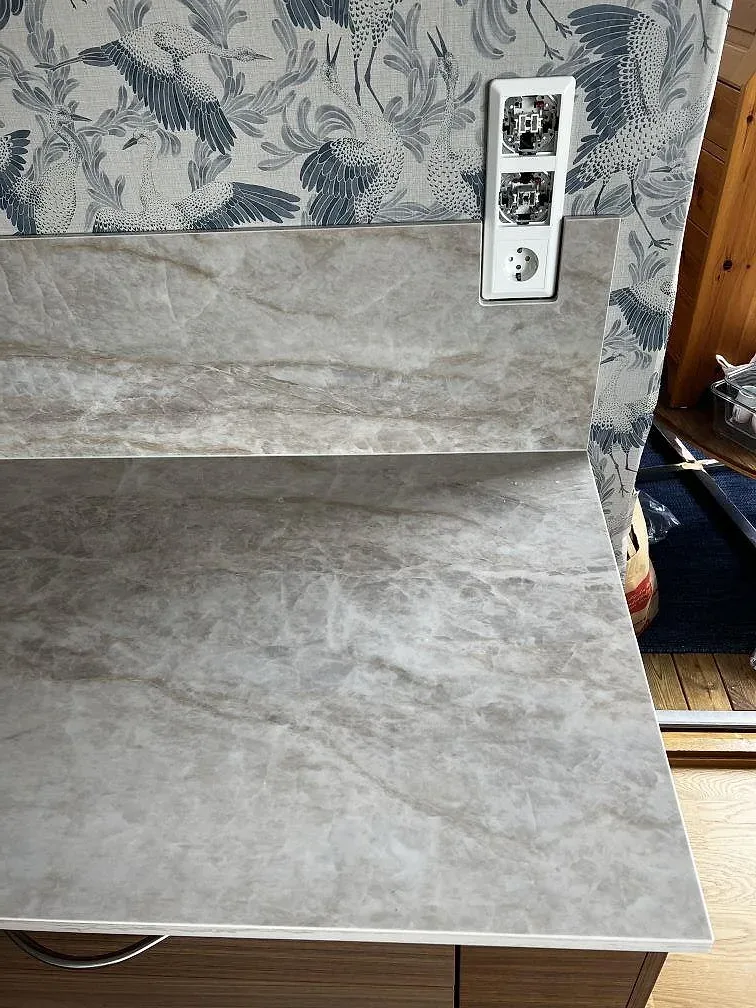 Detalj av uppvikt Dekton Arga i polerad keramik mot fågelmönstrad vägg i kök i Karlskrona.