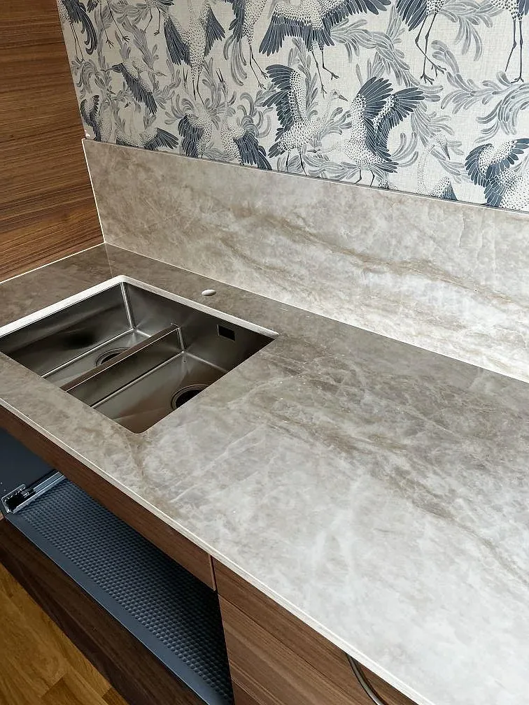 Diskhozonen i polerad Dekton Arga keramik med ljus grå ådring och valnötsfärgad köksinredning i Karlskrona.