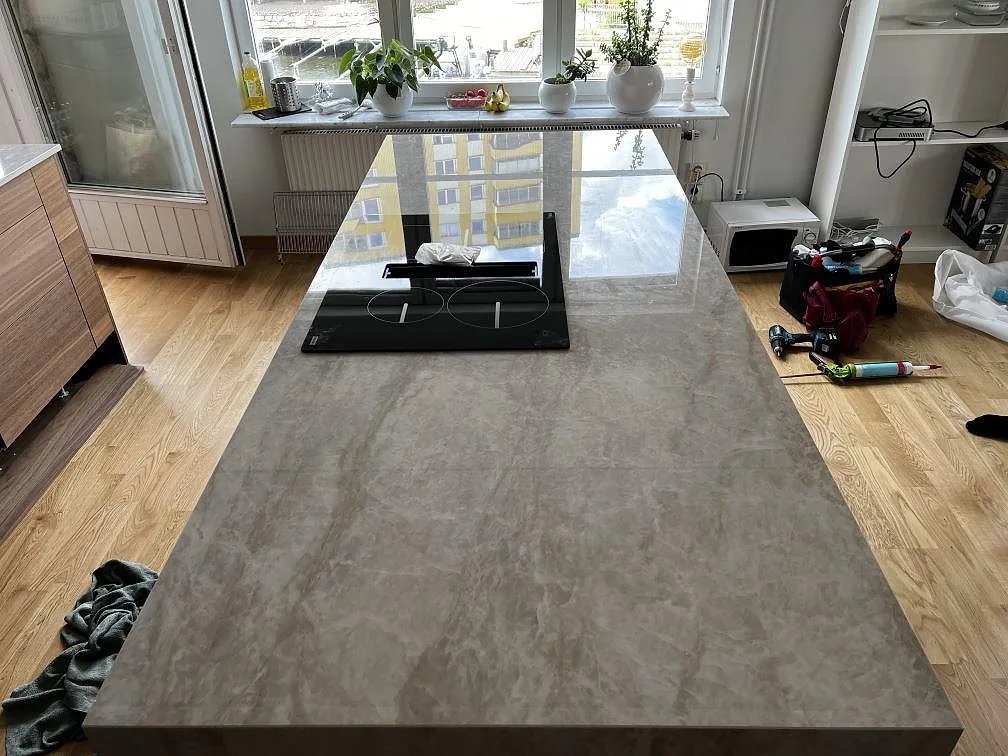 Köksö i polerad Dekton Arga keramik med infälld häll och ljus stenådring i ett kök i Karlskrona.