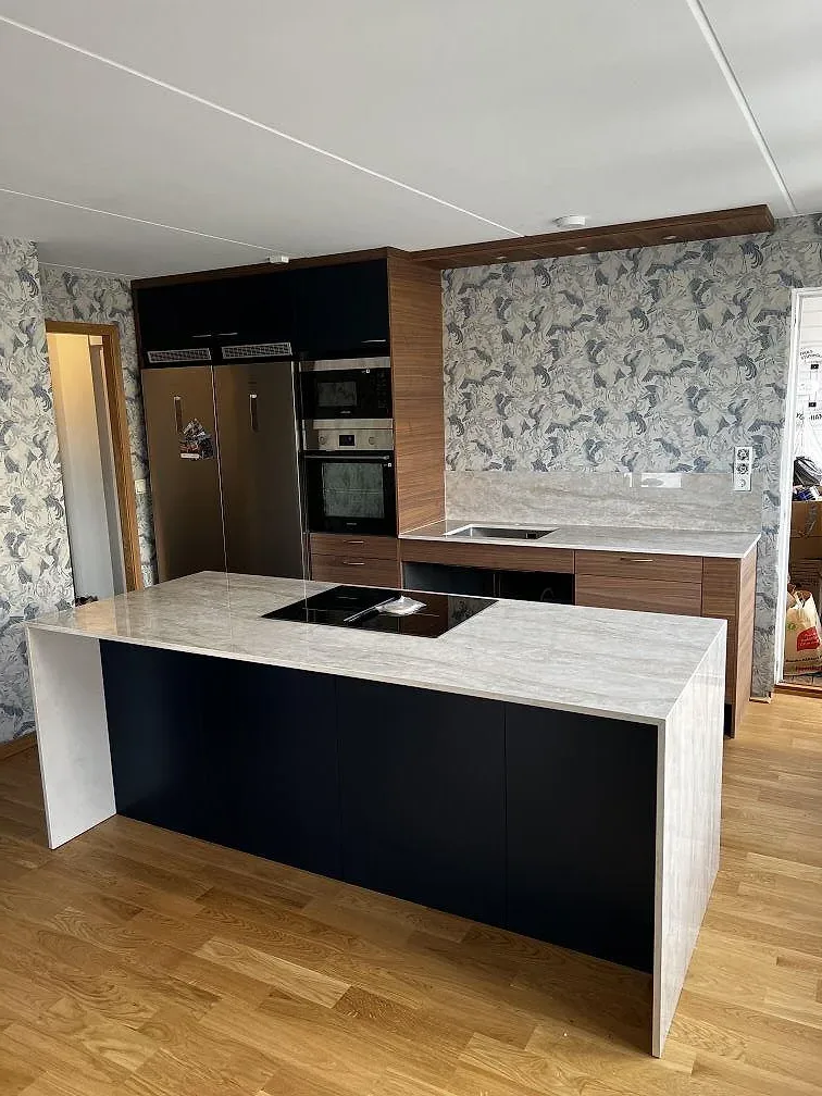 Polerad köksbänkskiva och köksö i Dekton Arga med valnötsfärgad inredning och fågelmönstrad vägg i Karlskrona.