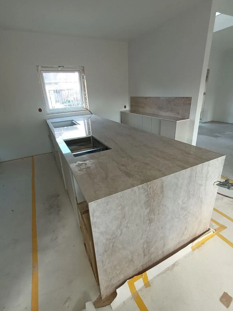 Polerad Dekton Arga keramik som köksö med vattenfallsida och stänkskydd under montering i Karlstad.