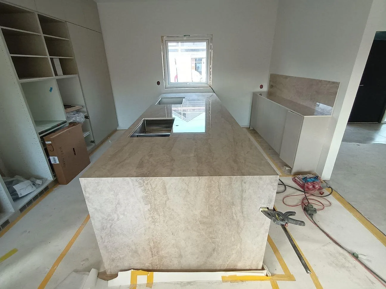 Köksbänkskiva i varm cremebeige Dekton Arga, polerad, på en lång köksö med nedfälld gavel och underlimmad rostfri diskho i ett kök i Karlstad.