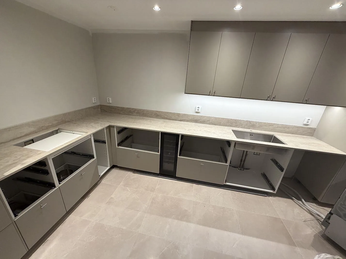 Köksbänkskiva i ljus Dekton Arga, polerad, i ett L-format kök i Karlstad med underlimmad rostfri diskho och uppvikt stänkkant, fotograferad under montering.