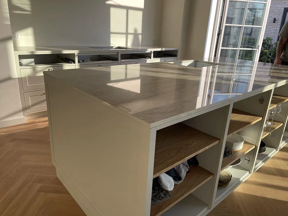 Sidovy av köksö i polerad Dekton Arga med travertinlik ådring, öppna hyllor och ljusinsläpp i Kastrup.