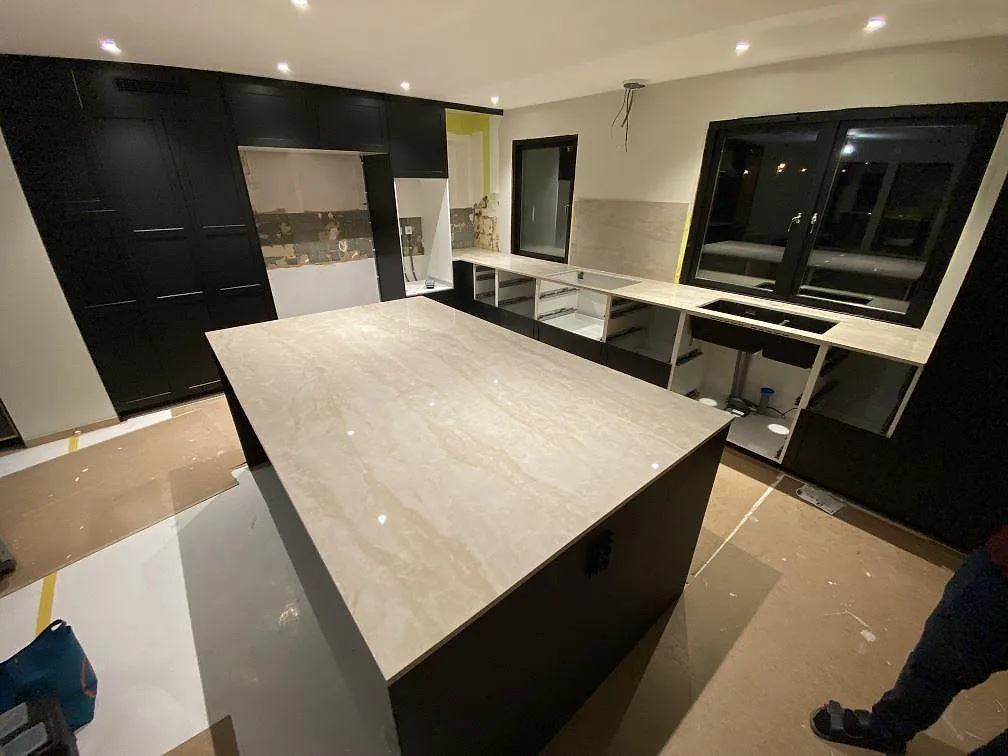 Krämvit köksö i Dekton Arga med kringgående bänk i samma keramik, mörka köksstommar och stort fönster, kök i Katrineholm.
