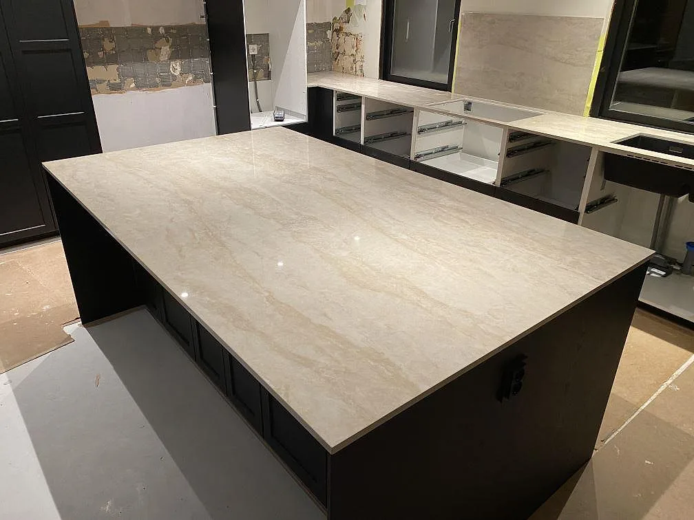 Köksbänkskiva och köksö i krämvit Dekton Arga, polerad keramik med mjuk ådring, i ett kök under montering i Katrineholm.